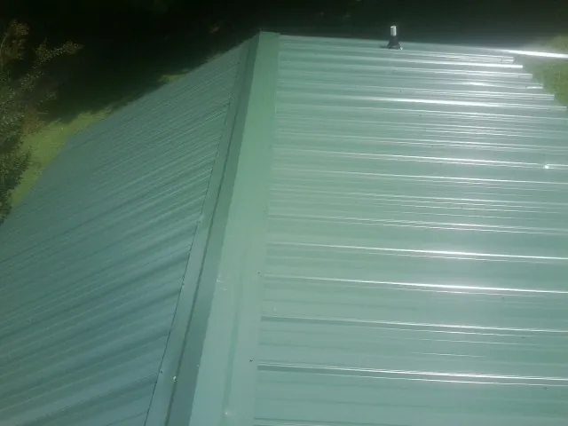 New green metal panels meeting at the ridge of a roof — Flat Roof Repair work by our crew in Cordova